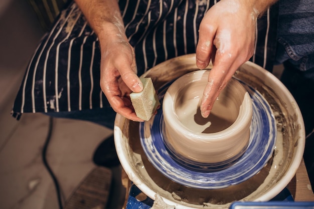 Partial view of young african american couple in aprons sculpting pot on wheel with wet sponge in pottery