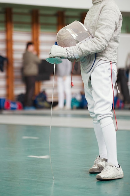 Participant of the fencing tournament with rapier and\
protective mask in hands