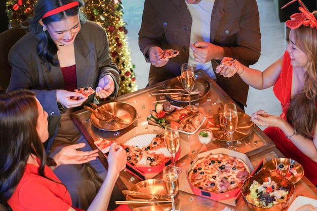 Partij van mooie Aziatische vriend vrouwelijke en mannelijke vieren. vrouw serveert pizza op tafel met hapje en drankje. geluk vrienden kerstavond viering etentje eten en champagne.