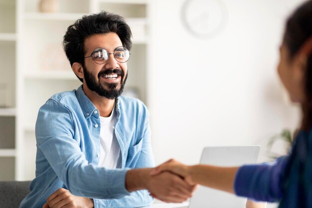 Partnership concept smiling indian male entrepreneur giving hand for handshake to female