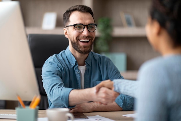 Partnership smiling male entrepreneur giving hand for handshake to female in office