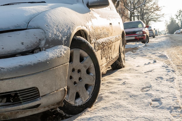 Части автомобиля покрыты снегом и льдом после снегопада Крупный план колес в грязи и противогололедных реагентах Большие морозы и много снега в городе Проблемы на зимних скользких дорогах