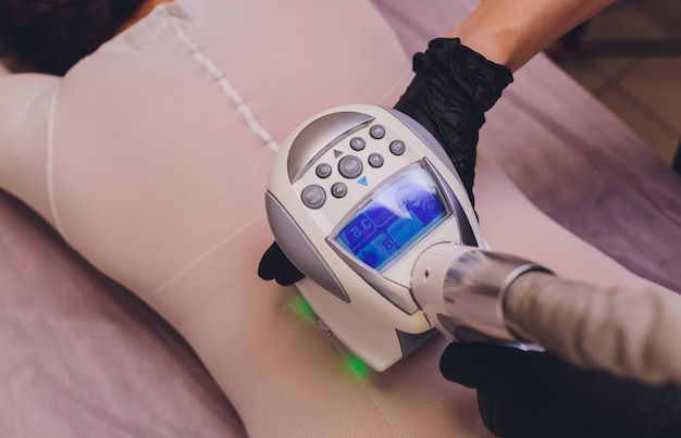 Photo parts of female body in special white suit having anti cellulite massage with spa apparatus