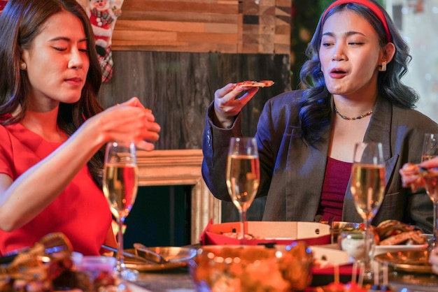 Party of beautiful asian friend female celebrating. women eating pizza on table with snack and drink. happiness friends christmas eve celebration dinner party food and champagne.