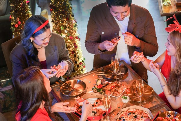 Party of beautiful asian friend female and male celebrating. woman serving pizza on table with snack and drink. happiness friends christmas eve celebration dinner party food and champagne.
