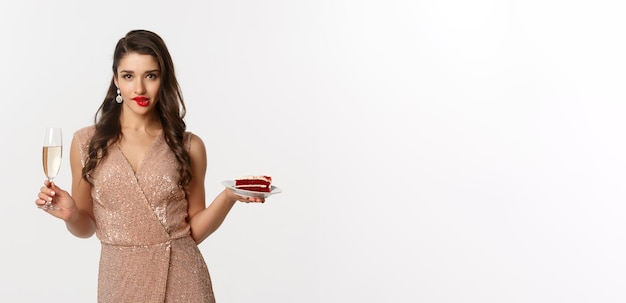 Party and celebration concept sexy woman in elegant dress holding champagne and piece of cake biting