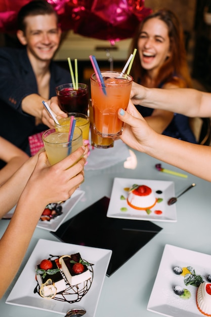 Photo party celebration with alcohol cocktail closeup. modern lifestyle. happy toast, youth company in cafe with drinks on focus on foreground. joyful leisure time, festivity concept