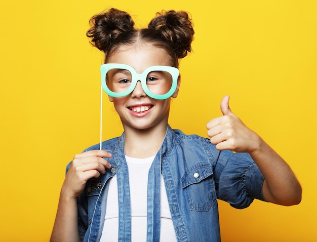 Party childhood and people concept little girl with a paper accessories over yellow background