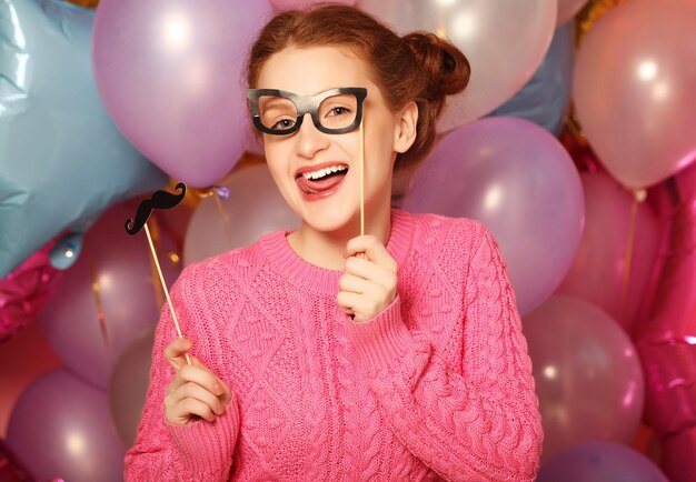 Party concept happy girl with fake mustaches and glasses Background of with many colorful balloons