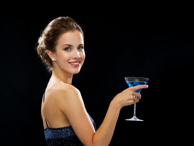 party, drinks, holidays, luxury and celebration concept - smiling woman in evening dress holding cocktail over black background