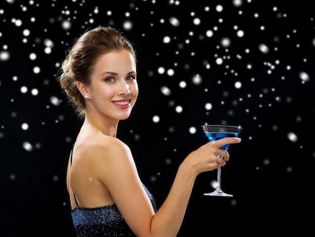 вечеринка, напитки, праздники, роскошь и концепция праздника - улыбающаяся женщина в вечернем платье с коктейлем на черном снежном фоне