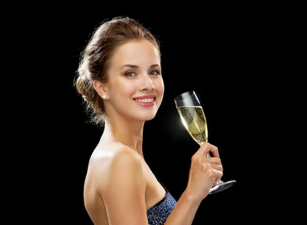 party, drinks, holidays, luxury and celebration concept - smiling woman in evening dress with glass of sparkling wine over black background