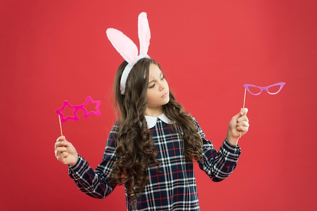 Party Element. teen kid in rabbit costume having fun. happy easter. small girl wear bunny ears on Easter day. serious child choose party glasses. Easter bunny rabbit with ears. Kid on Easter egg hunt.