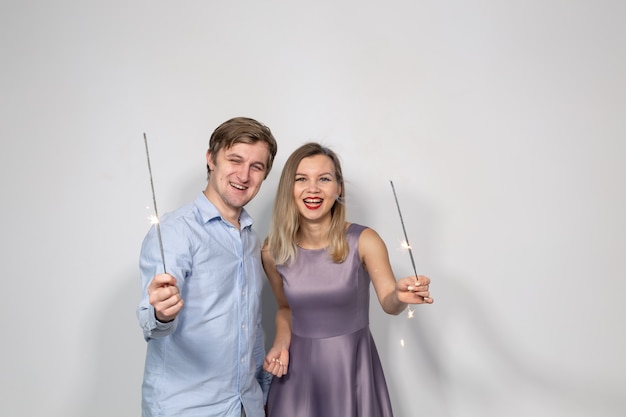 Party, family and holidays concept - young couple looking to sparklers on white wall.