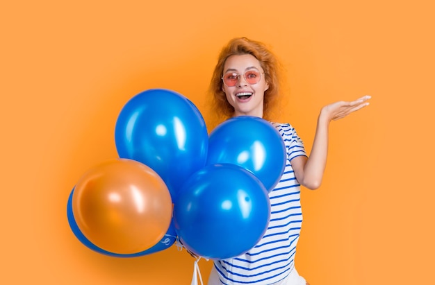 Партийная девушка с воздушным шаром в солнцезащитных очках удивленная девушка держит партийные воздушные шары в студии девушка с повітряным шаром для вечеринки изолирована на желтом фоне