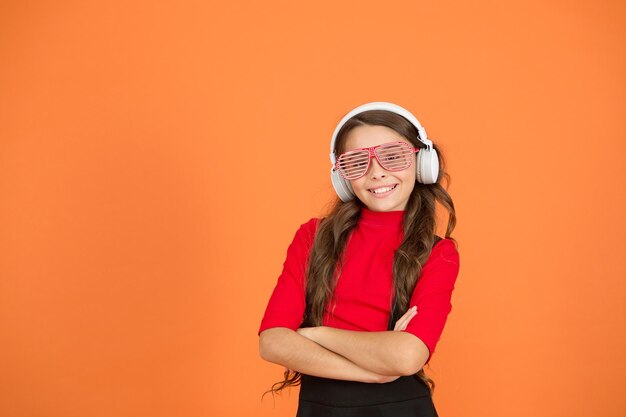 Party in her head. Party accessory. Having fun. Play list for party. Music concept. Kid wear eyeglasses. Eyewear fashion store. Girl with eyeglasses orange background. Event and entertainment.