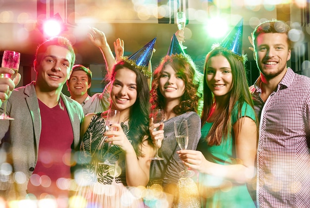 Photo party, holidays, celebration, nightlife and people concept - smiling friends in party caps with glasses of champagne in club