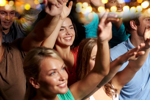 party, holidays, celebration, nightlife and people concept - smiling friends waving hands at concert in club