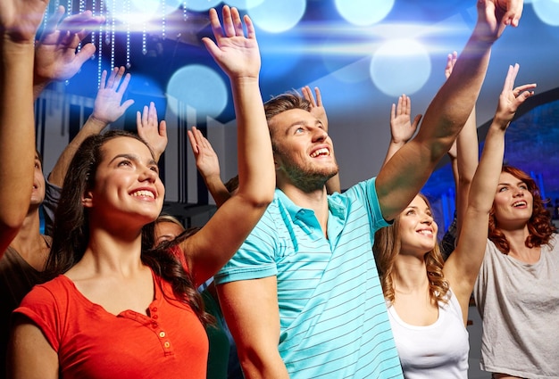 party, holidays, celebration, nightlife and people concept - smiling friends waving hands at concert in club