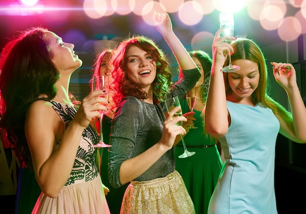 party, holidays, celebration, nightlife and people concept - smiling friends with glasses of champagne dancing in club