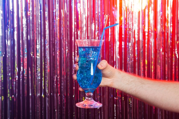 Party holidays and drink concept  blue cocktail in a male hand on a shiny background