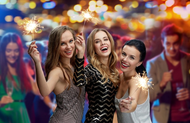 party, holidays, nightlife and people concept - happy young women with sparklers at night club over lights background