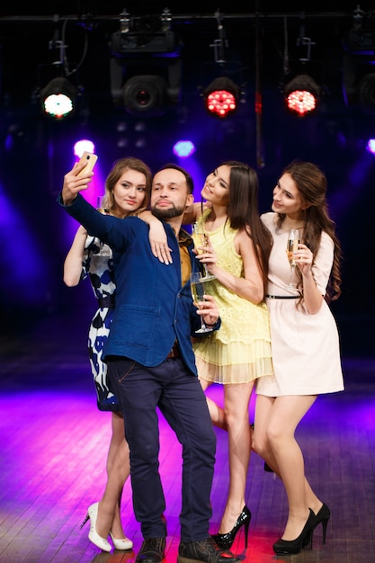 Concetto di festa, vacanze, tecnologia, vita notturna e persone - amici sorridenti con bicchieri di champagne e smartphone che prendono selfie nel club