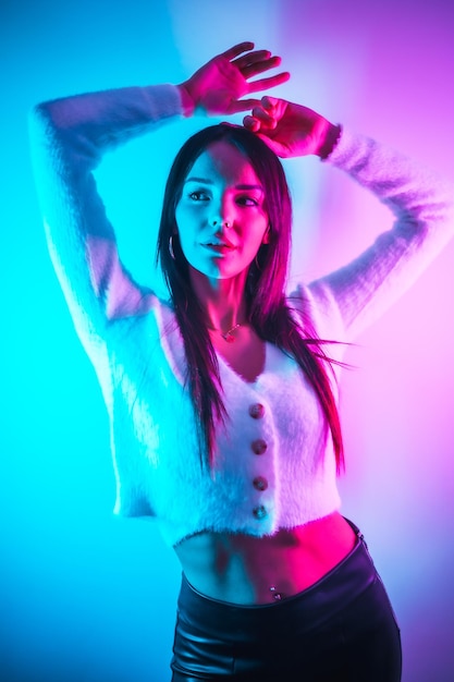 Party lifestyle in a nightclub with pink blue neon lights portrait of a young brunette Caucasian woman in a white wool sweater