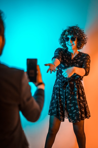 Party lifestyle, a young man records a video of a young woman dancing at a party with orange and blue lights