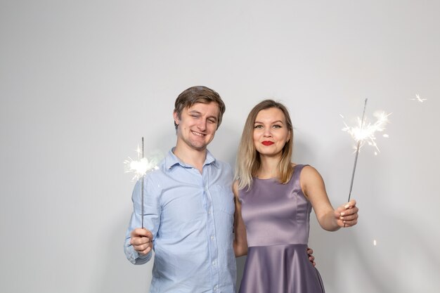 Party, new year, christmas, family and holidays concept - young couple holding sparklers on white background