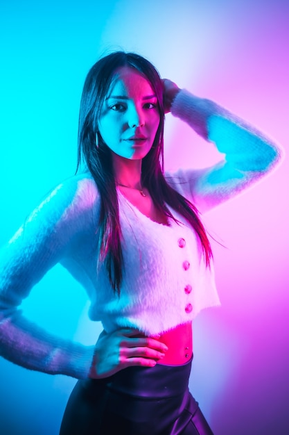 Party in a nightclub with pink blue neon lights, a young brunette Caucasian woman in a white wool sweater, vertical photo