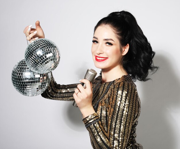 Party photo of young sensual brunette woman wearing evening dress and holding disco balls