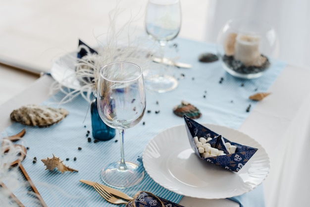 Party table setting in sea style. Elegant plates, glasses, in bluÑ colors. Paper boats with marshmallow. Birthday or baby shower boy concept.