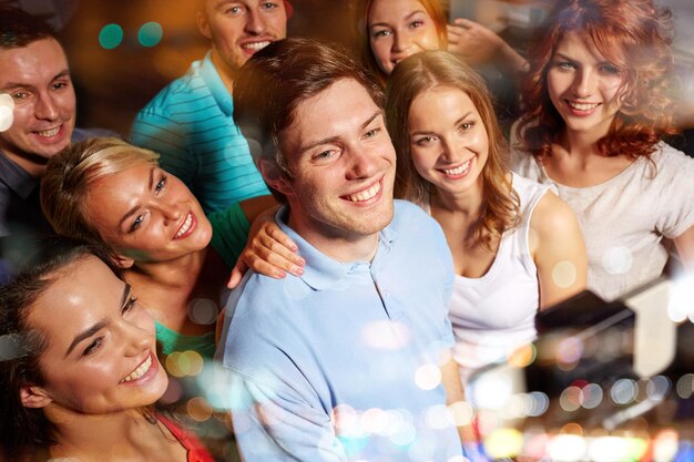 party, technology, nightlife and people concept - smiling friends with smartphone and monopod taking selfie in club