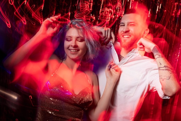 Party vibe Excited couple Birthday fun Festive celebration Happy expressive man and woman enjoying holiday long exposure black red light motion ornament waves blur