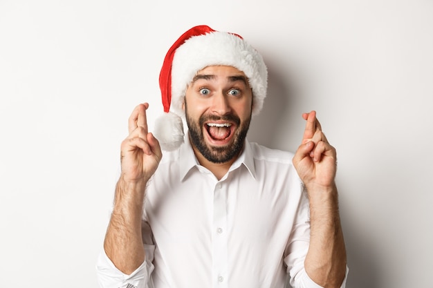 파티, 겨울 휴가 및 축하 개념. 크리스마스 소원을 만드는 산타 모자에 행복 한 사람, 행운을 위해 손가락을 교차 하 고 흥분, 흰색 배경을 찾고.