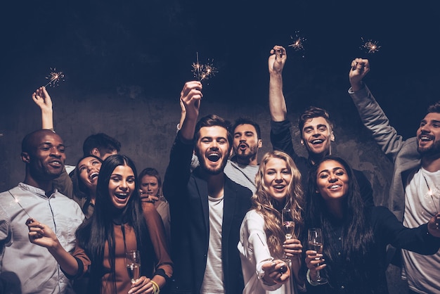 Party with friends. Group of cheerful young people carrying sparklers and champagne flutes