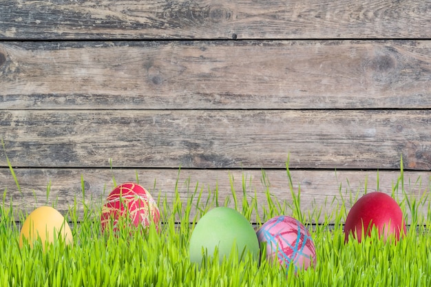 Pasen achtergrond met eieren in gras en bloemen, houten achtergrond