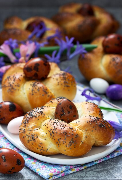 Pasen-broodjes, gekleurde eieren en bloemen op een grijze concrete achtergrond.