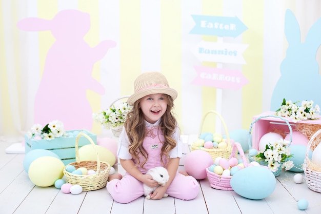 Pasen concept en familievakantie! klein meisje spelen met paashaas. Pasen kleurrijke decor in huis, een mand van kleurrijke eieren. Een meisje jaagt op paaseieren. Meisje dat een konijn in zijn handen houdt.