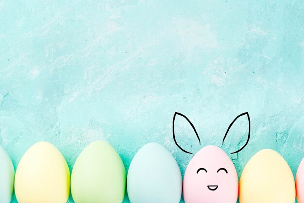 Pasen-concept, pastelkleurige eieren op een lichtblauwe achtergrond, met geschilderde konijnsnuiten en oren. Achtergrond voor wenskaart, kopie ruimte