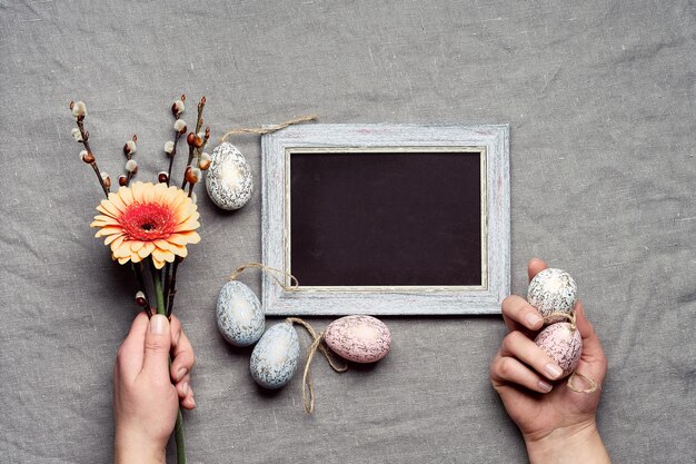 Pasen decoratie tekst Happy Easter op blackboard krijtbord handen met bos bloemen met gerbera en pussy willow en hout paaseieren aarde gekleurde linnen textiel achtergrond