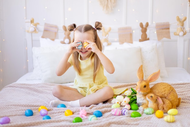 Pasen een klein meisje met geschilderde gekleurde eieren tulpen en een konijn thuis in een lichte kamer bereidt zich voor op de vakantie glimlachend plezier maken en spelen met eieren haar ogen sluiten