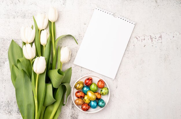 Pasen en lente concept. Bovenaanzicht van witte tulpen, lege kalender en gekleurde paaseieren op betonnen backgrund