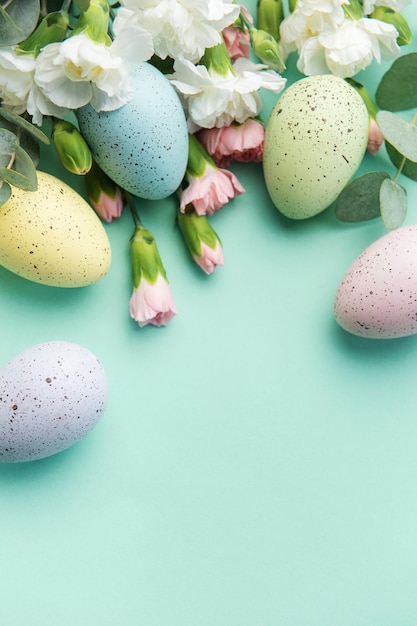 Pasen gekleurde eieren en een boeket van witte en roze anjers met eucalyptustakken op een zachtgroene achtergrond