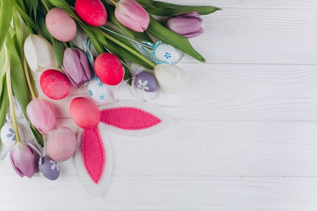 Pasen-samenstelling met gekleurde eieren, konijnoren en tulpen