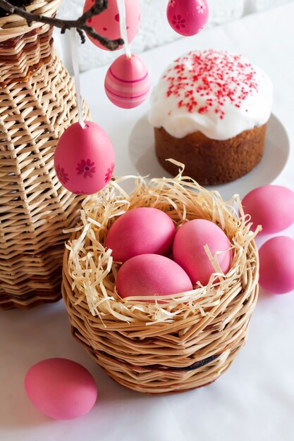 Pasen-samenstelling met roze gekleurde eieren in rieten mand en pasen-cake