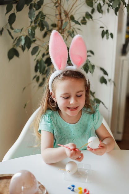 Pasen Schattig klein meisje in konijnenoren versiert paaseieren aan tafel thuis Lentevakantie