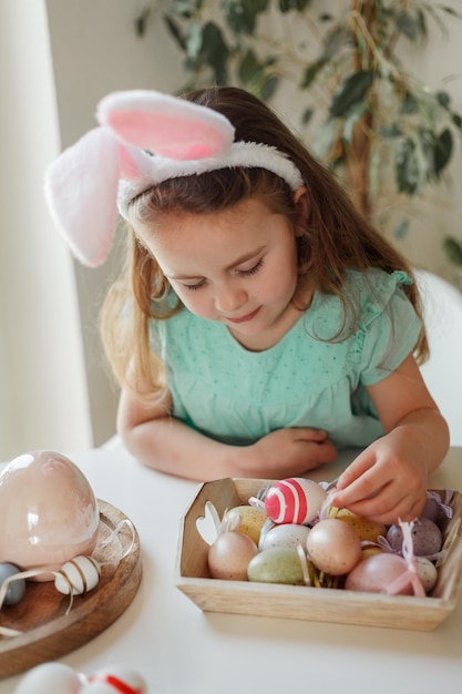 Pasen Schattig klein meisje in konijnenoren versiert paaseieren aan tafel thuis Lentevakantie