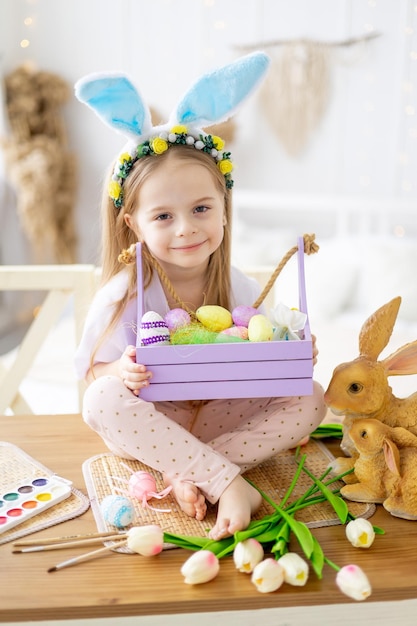 Pasen schattig klein meisje kind met bunny oren op haar hoofd spelen met kleurrijke paaseieren op een tafel in een lichte kamer levensstijl